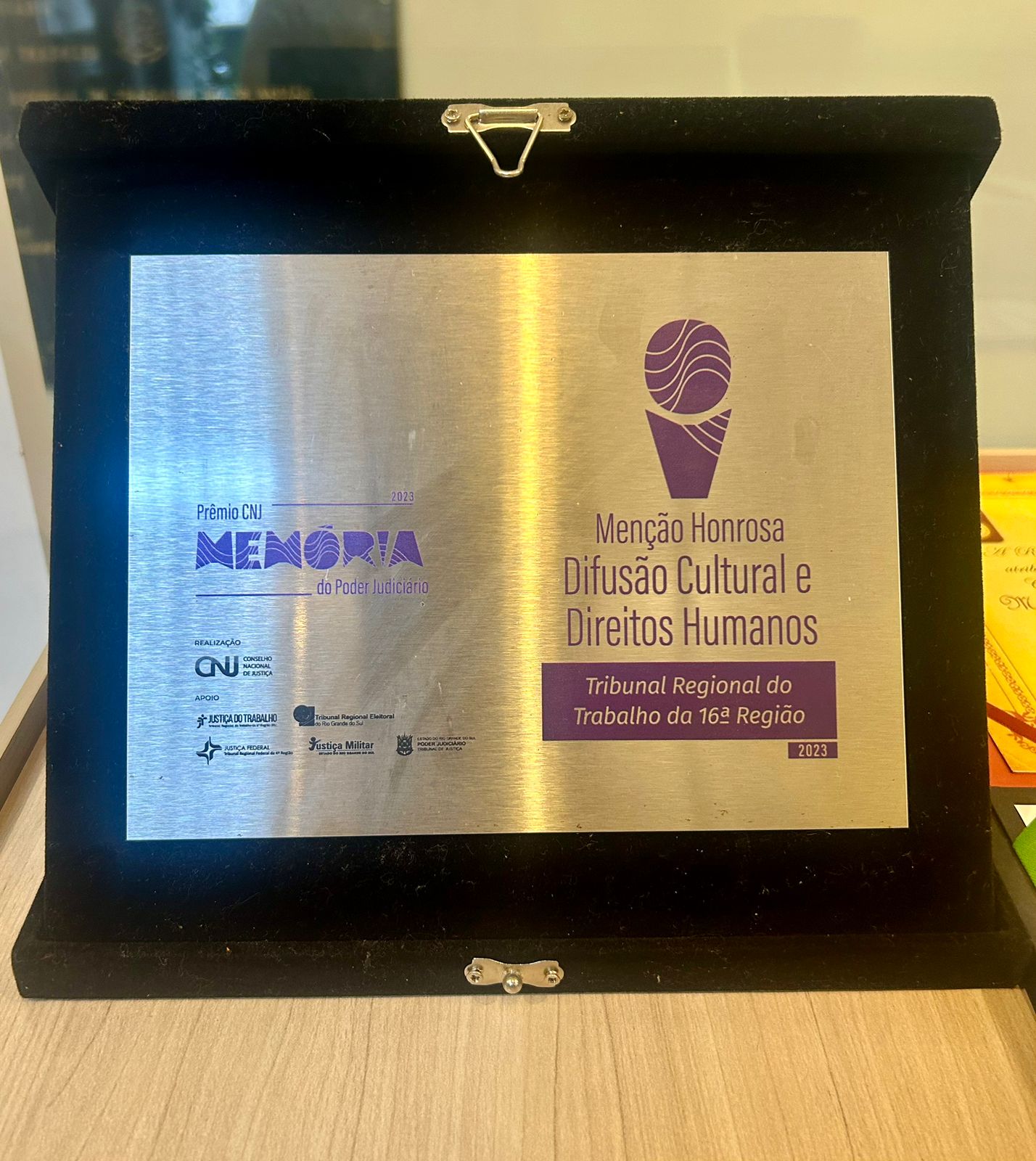 Placa metálica com letras na cor azul apoiada em base na cor preta