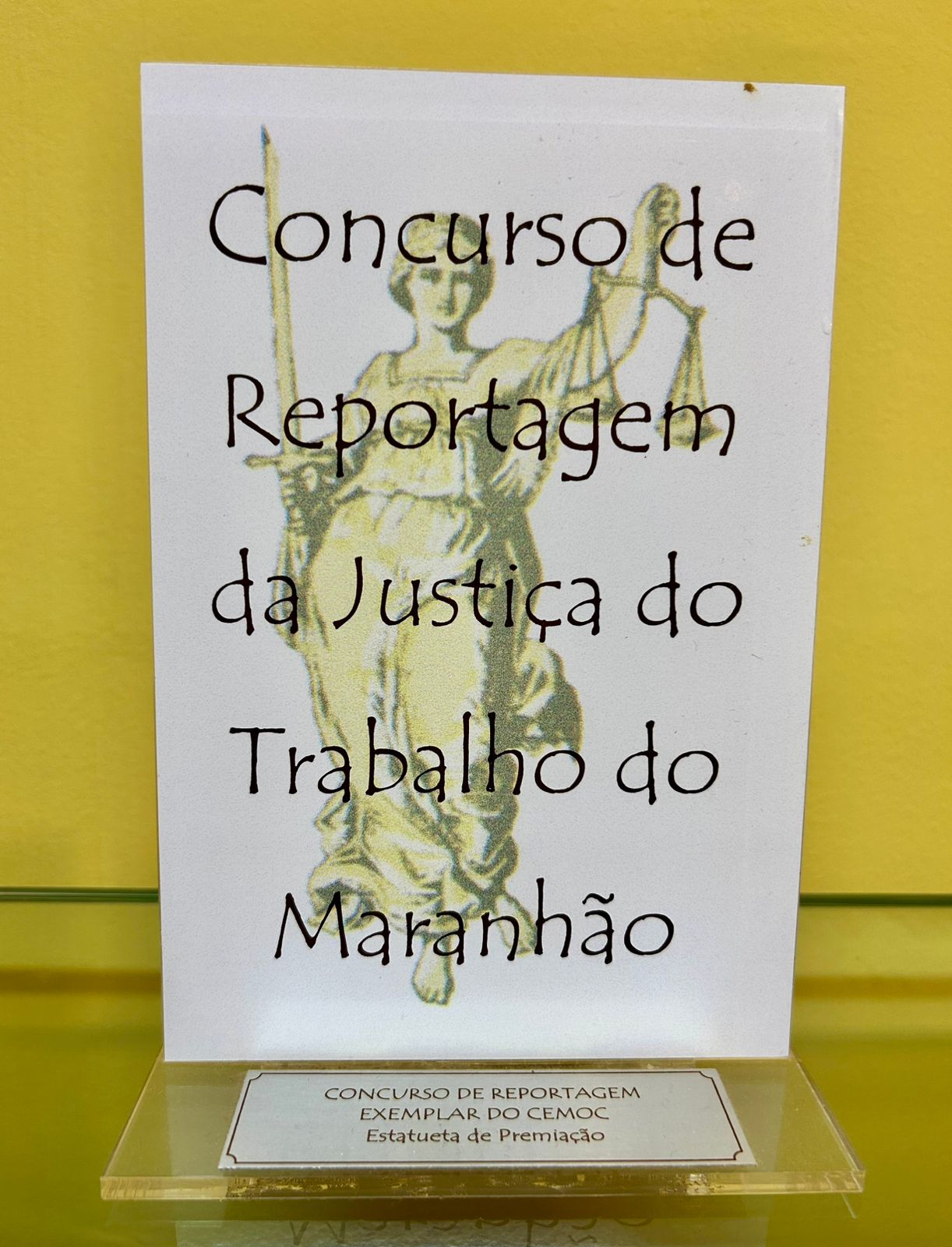 Prêmio na cor branca com letras na cor preta e apoiada em base de acrílico