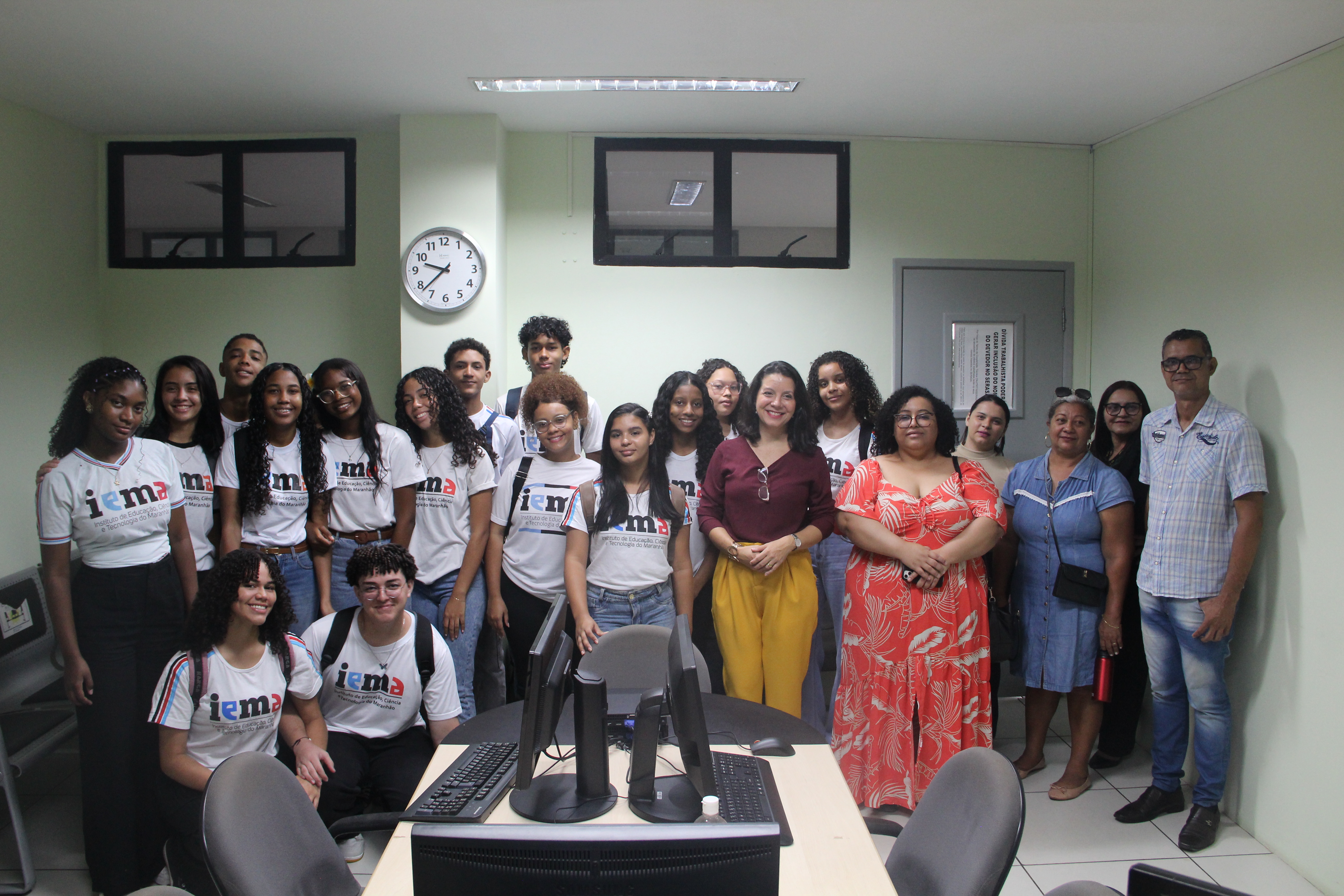 Foto mostra estudantes e professores do IEMA Itaqui-Bacanga ao lado da juíza Carolina Burlamaqui em uma sala de audiências no Fórum Astolfo Serra.