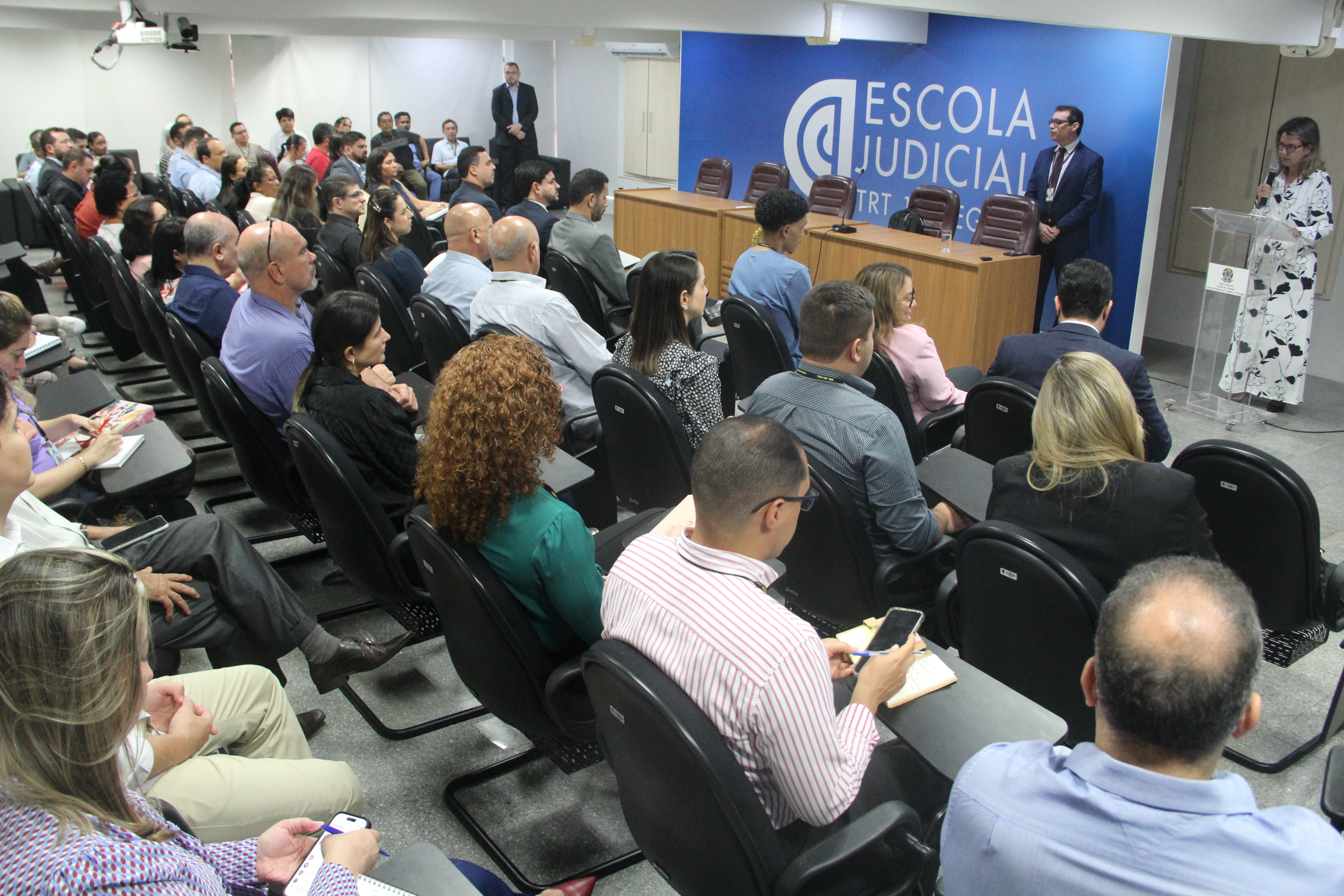 Foto mostra o auditório da EJUD cheio de servidores do TRT16. No canto superior direito a presença da presidente Desa. Márcia Andrea Farias falando para o público presente. Ao lado dela o palestrante Flávio Marcílio.