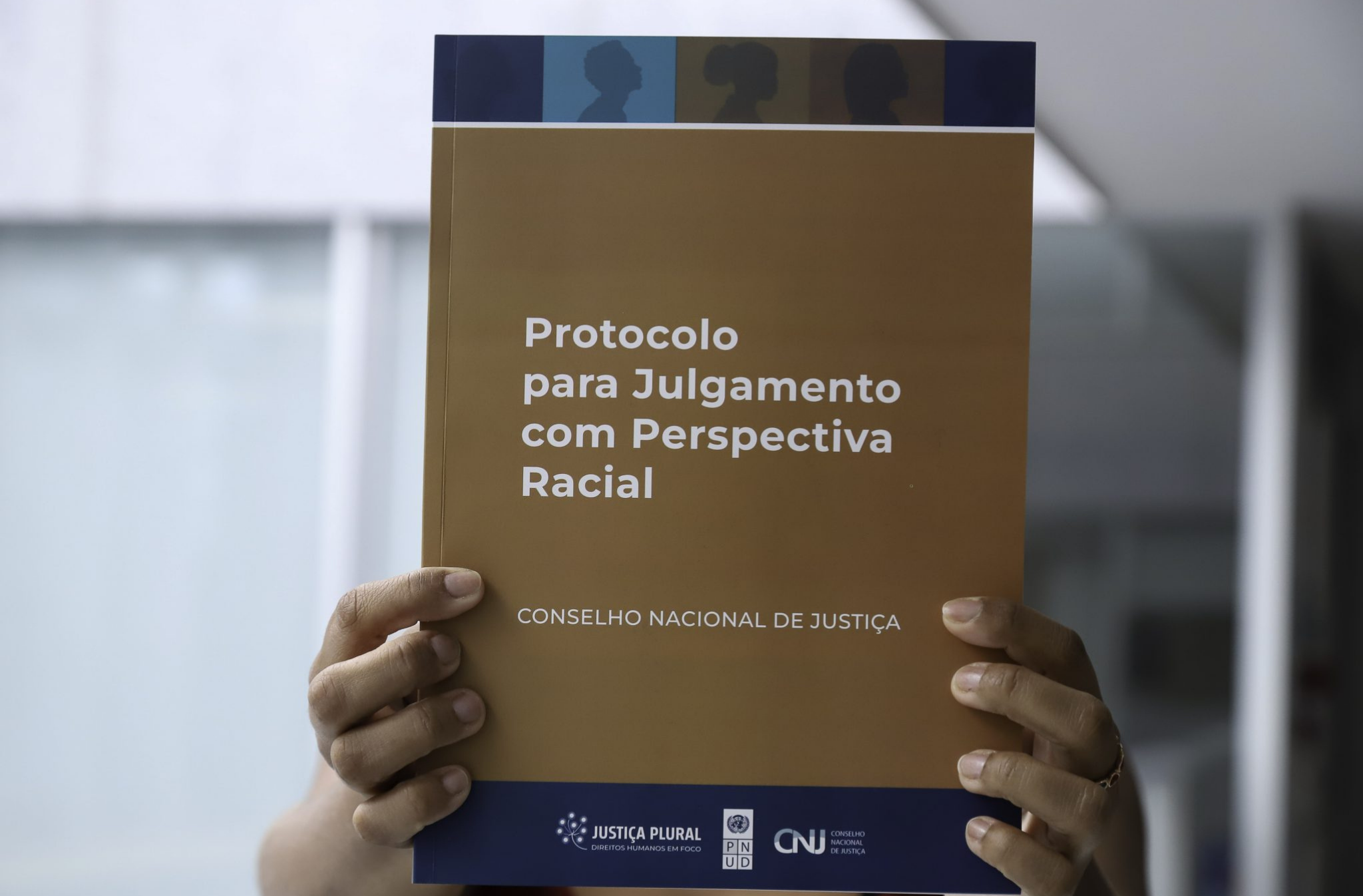 Arte feita com uma foto de uma pessoa negra segurando um livro: a capa tem a informação - Protocolo de Julgamento com Perspectiva Racial - CNJ