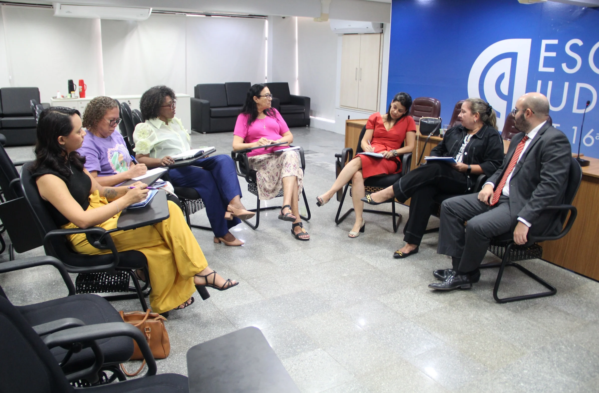 Foto mostra um reunião de pessoas. Todas estão sentados na cadeiras posicionadas em formato de meia lua no centro do auditório da Escola judicial do TRT-16