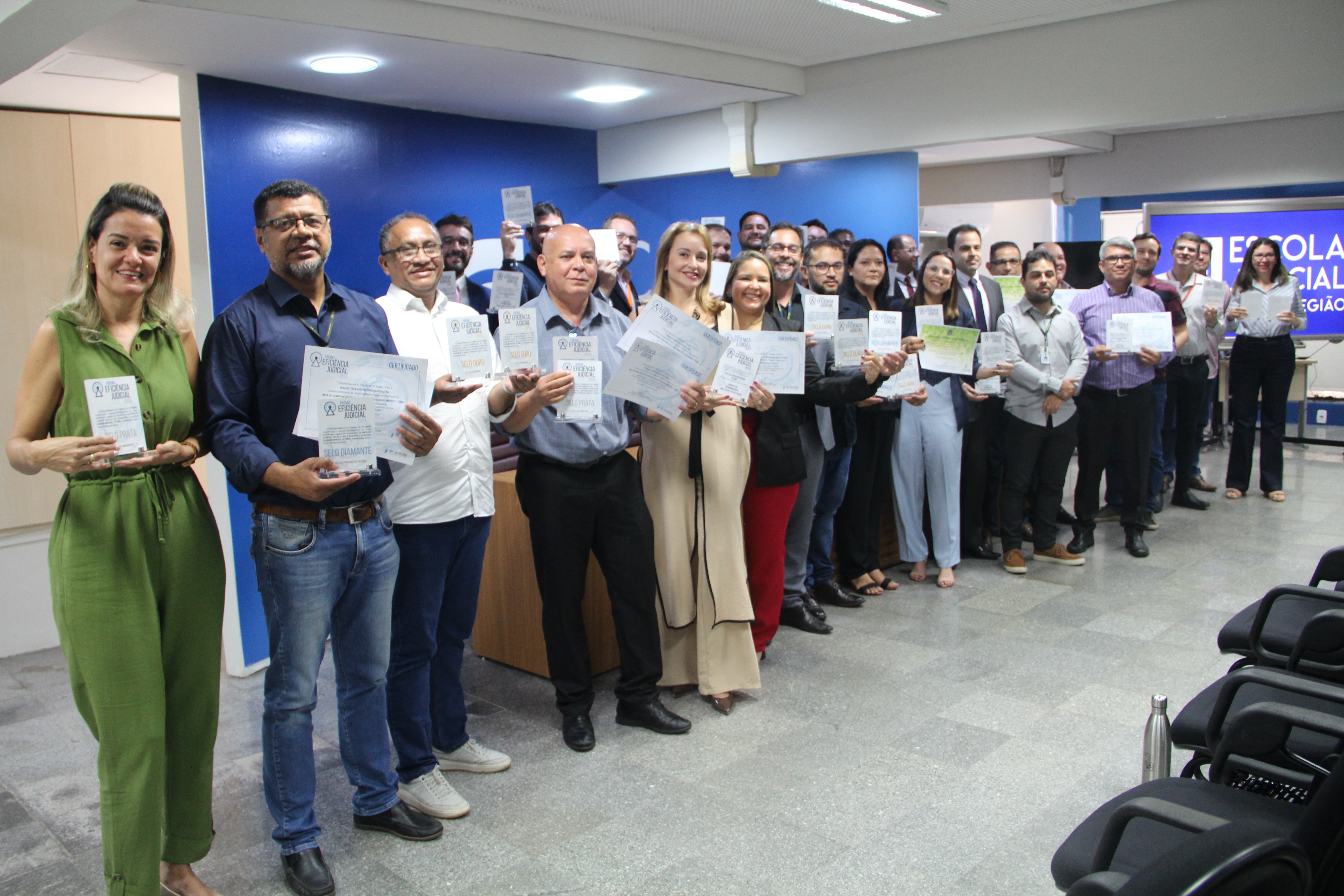 Foto mostra servidores que atual no 1º e 2º Graus da Justiça do Trabalho no Maranhão. Eles estão em pé e perfilados, cada um segura um troféu e um certificado.