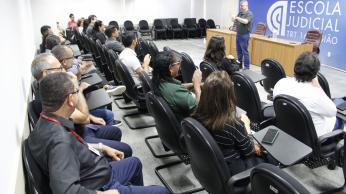 Foto mostra um homem em pé diante de várias pessoas sentadas em um auditório. 