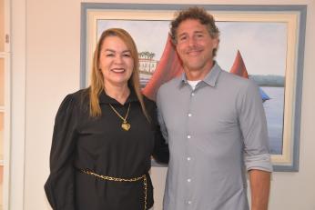 Foto mostra uma mulher e um homem, um ao lado do outro. Estão em pé.