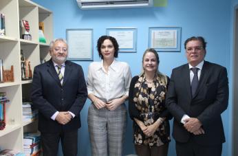 Foto mostra dois homens e duas mulheres em pé. Ao fundo uma parede azul. Na esquerda uma esquerda.