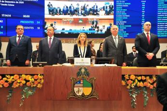 Foto mostra cinco pessoas em pé atrás de uma mesa de honra. Na parte da frente, o brasão do Poder Legislativo
