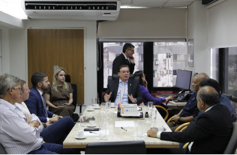 Foto mostra uma reunião de pessoas. Todos estão sentados em volta de uma mesa.