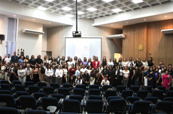 Foto mostra várias pessoas em pé, no palco de um auditório