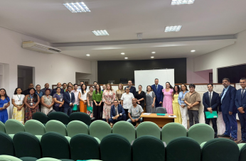 Foto mostra várias pessoas em pé, na parte de frente de um auditório.