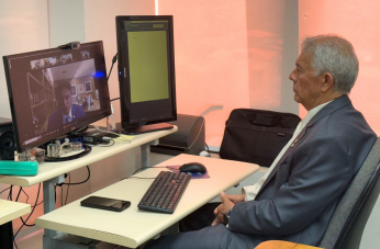 Foto mostra um homem sentado em uma cadeira, diante de um computador. Ele participa de uma reunião online. 