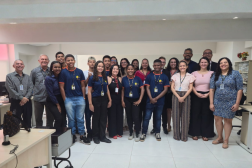 Foto mostra várias pessoas em pé, posicionadas dentro de uma sala. São homens e mulheres, além de jovens que integram o programa Programa de Aprendizagem Profissional Inclusiva.