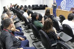 Foto mostra um homem em pé diante de várias pessoas sentadas em um auditório. 