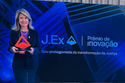 Foto mostra uma mulher segurando um troféu de acrílico. Ao lado a informação. J.Ex. Prêmio de Inovação