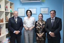 Foto mostra dois homens e duas mulheres em pé. Ao fundo uma parede azul. Na esquerda uma esquerda.