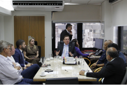 Foto mostra uma reunião de pessoas. Todos estão sentados em volta de uma mesa.