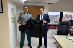 Foto mostra dois homens em pé, um ao lado do outro. Eles seguram uma camisa de combate. 