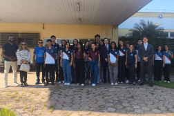 Foto mostra várias pessoas reunidas em frente a um prédio. Elas estão posicionadas um ao lado da outra.