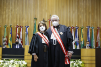 Imagem de parte do Plenário, com fundo em madeira, onde estão alinhadas várias bandeiras, dois homens sentados na bancada e ao centro a ministra Maria Cristina Peduzzi e o ministro Emmanoel Pereira 