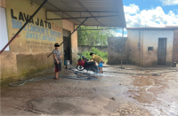Imagem de lava a jato onde se vê um adolescente em pé e outro lavando uma moto.