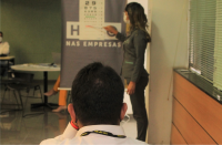 Foto de servidor, de costas, fazendo exame oftalmológico com a ajuda de uma moça, usando roupa verde.