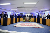 mesa de honra em plenário composto por autoridades. ao meio, tapete vermelho em piso de carpete azul