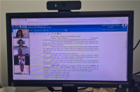 Foto de uma tela de computador onde há uma mulher e quatro homens à esquerda, em sentido vertical. No centro da tela de computador, texto referente à ata de audiência. Acima, barra azul com outras informações processuais.