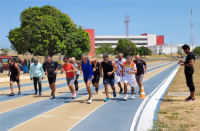 Fotos de vários homens e de uma mulher vestindo roupas esportivas, que estão correndo numa pista de atletismo. À direita, há um homem em pé vestindo roupas pretas cronometrando a atividade.