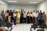 A imagem mostra a Desembargadora Solange Castro, diretora da Ejud, ladeada de servidores do Polo Timon. Todos estão em pé. Ao fundo imagens das bandeiras do Brasil e do Maranhão.