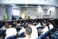 Imagem de um auditório com estudantes na plateia. Ao fundo, imagens do palestra Juiz Auxiliar da Corregedoria, Saulo Fontes.