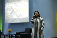 Imagens da palestrante Scheila Alves Vale professora do IFMA. Ao fundo painel de apresentação