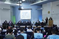 Foto de auditório com autoridades em destaques no palco e pessoas assistindo a palestra