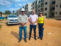 Imagem mostra em primeiro plano, três pessoas em pé diante de uma canteiro de obras. Ao fundo, imagens de prédios residenciais em construção.