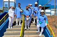 Foto de oito pessoas usando roupas de proteção e capacetes, posicionadas de pé numa escada de cimento com corrimãos amarelos. Todos posam para a câmera sorrindo.