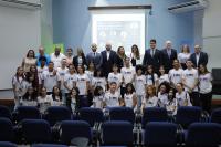 Pessoas em pé, posicionadas para foto e ao fundo imagem do telão com a apresentação do evento