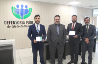 Foto mostra 4 homens perfilados um ao lado do outro. Ao fundo, a logomarca e a identificação da Defensoria Pública do Estado do Maranhão.