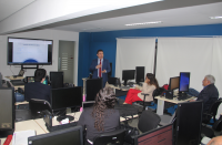 Imagem mostra uma sala com pessoas sentadas. Ao fundo, um homem em pé ministra uma aula.