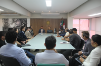 Foto mostra várias pessoas sentadas em volta de uma mesa de reuniões, durante audiência durante audiência de conciliação