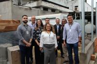 Foto mostra pessoas em pé, posicionadas em uma canteiro de obras. E ao fundo um gerador de energia. No centro da foto a Diretora-Geral Fernanda Muniz em sua volta servidores e servidoras. 