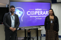 Foto mostra um homem e uma mulher posicionados um de cada lado de um painel escrito Prêmio Cooperari