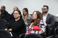 Foto mostra homens e mulheres sentados em cadeiras no auditório da Ejud-16. 