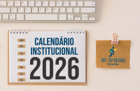 Arte com fundo cor de areia, tendo ao topo parte do teclado. Abaixo dele, um calendário de mesa com espiral, onde se lê CALENDÁRIO INSTITUCIONAL 2026. À direita, clipe rosado segurando uma folhinha de papel pardo, onde aparece a logomarca do TRT-16.