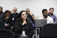 Foto mostra pessoas sentadas com as mãos na altura do rosto fazendo sinais de Libras