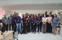 Foto mostra várias pessoas em pé, posicionadas dentro de uma sala. São homens e mulheres, além de jovens que integram o programa Programa de Aprendizagem Profissional Inclusiva.