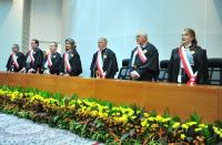 Foto de sete pessoas, de pé atrás de uma mesa de madeira. Flores amarelas na base da mesa.