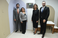 Foto mostra quatro pessoas em pé. São dois homens e duas mulheres. Ao fundo uma placa inaugural posicionada na parede.