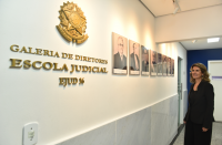 Foto mostra uma mulher em pé, olhando uma galeria de fotos. No primeiro plano a informação: Galeria de Diretores Escola Judicial.
