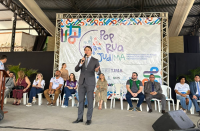 Foto mostra um homem de terno, em pé. Ao fundo um painel com a informação: Pop Rua Jud/MA