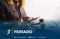 Foto parcial de uma mulher de cabelos claros, usando blazer marrom, segurando um celular na mão esquerda e um martelo de juiz na mão direita, em frente a um notebook aberto. Ao seu lado, vê-se uma balança, representando a Justiça. Em primeiro plano, uma tarja azul com o texto branco FERIADO NA VT ao lado da logomarca do TRT-16. Abaixo do texto, os ícones e endereços do TRT-16 nas redes sociais.