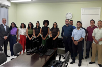 Foto mostra um grupo de pessoas, entre homens e mulheres, posicionados em pé em uma sala de audiências.